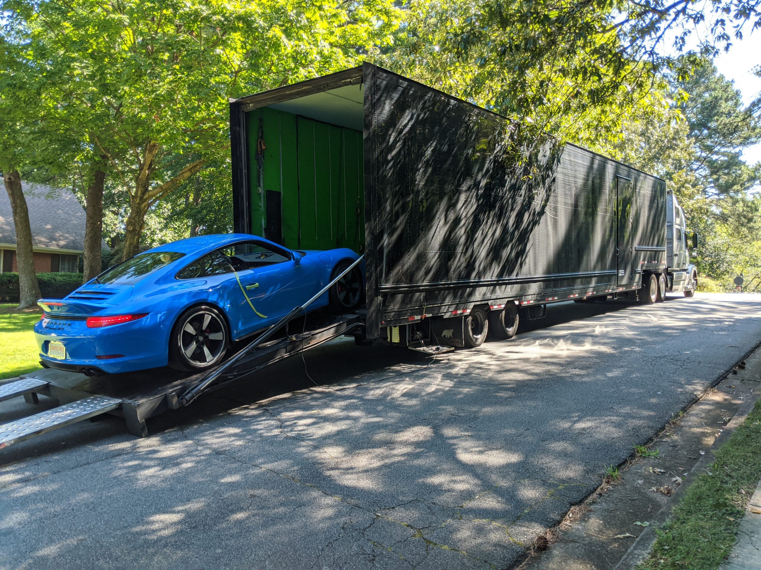 A 2016 VooDoo Blue Porsche 911 Carrera GTS being unloaded from a truck.